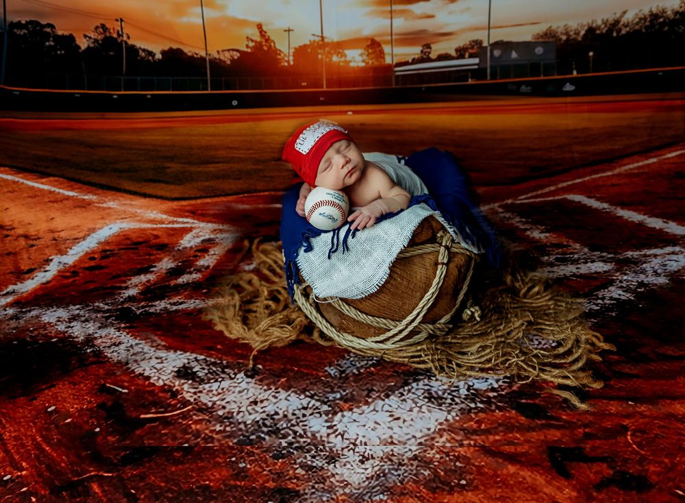 A baseball player wearing a Santa hat lies asleep on home plate at sunset with their glove and equipment.