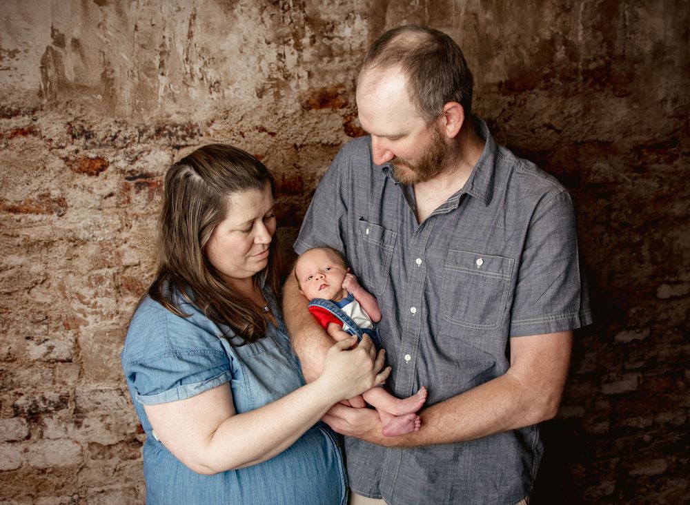 Parents share tender moments with their newborn baby in a rustic brick wall setting during a lifestyle photography session.