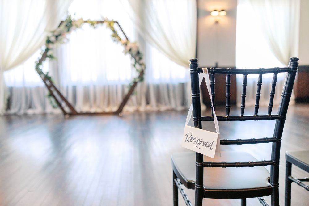 Black chiavari chairs with white sashes arranged in rows for an elegant indoor wedding ceremony.
