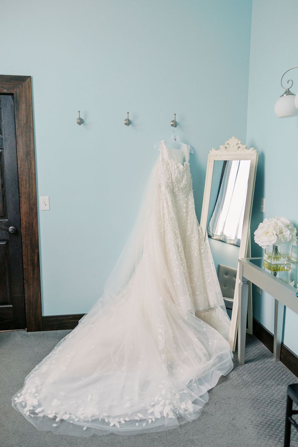 A long white lace wedding dress with cathedral train displayed on floor against light blue walls in varying angles.