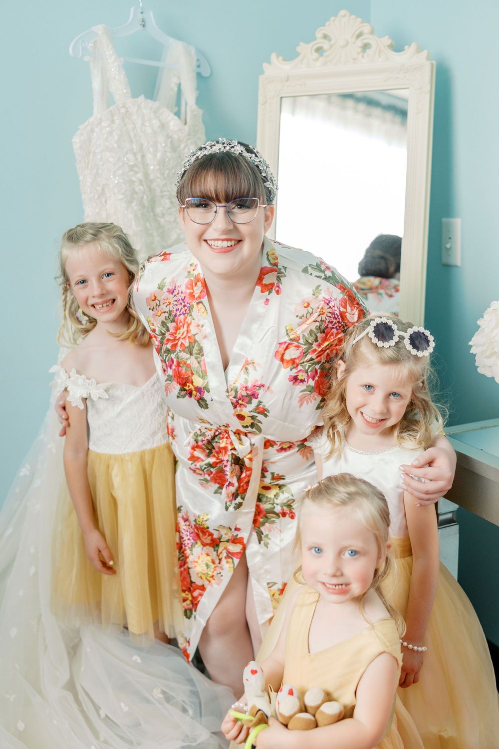 A group poses together in a room with a floral robe and yellow tulle skirts against a blue wall with an ornate mirror.