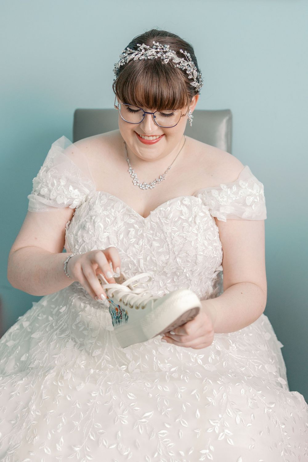 Wedding photograph showing someone wearing a beautiful white lace gown with glasses and delicate crystal headpiece.