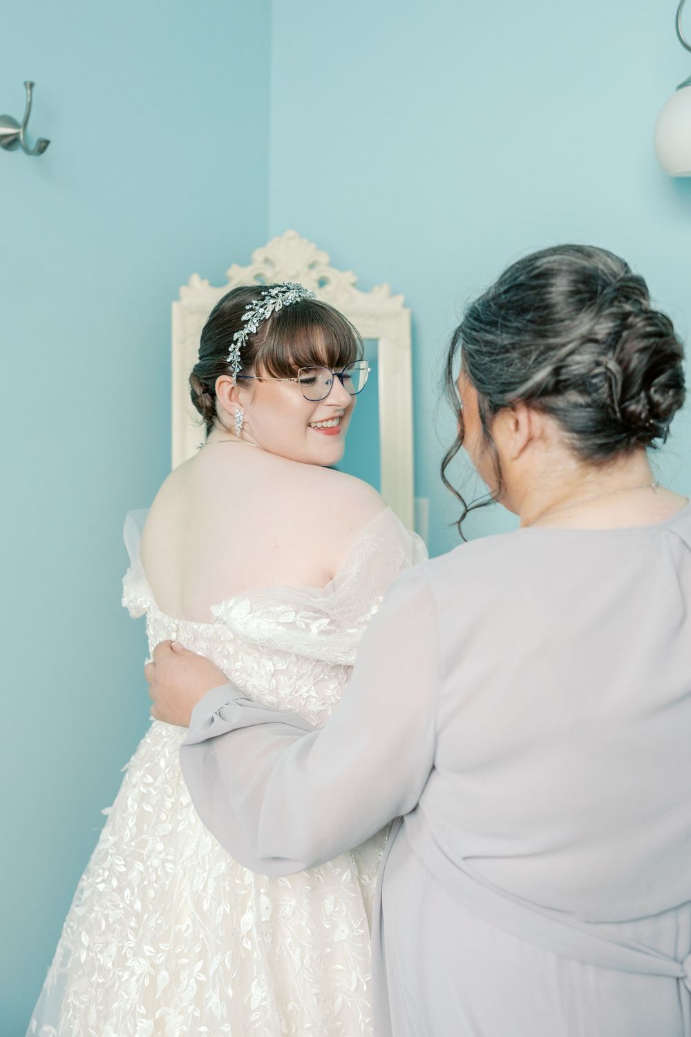 Three images show the back view of a bride and bridesmaid in gray and white dresses against a soft blue wall.