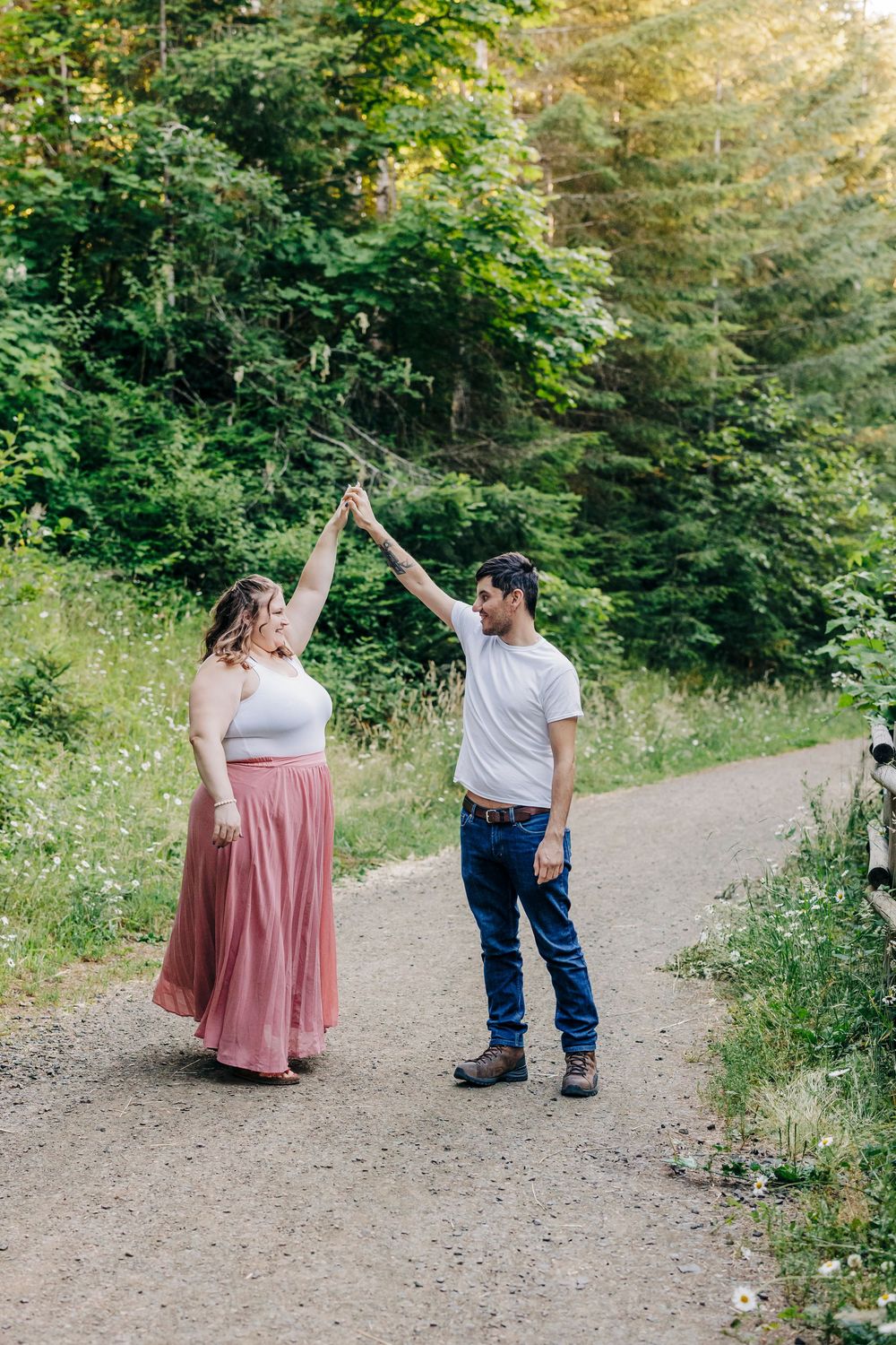 A couple dances playfully on a forest path surrounded by summer greenery and wildflowers.