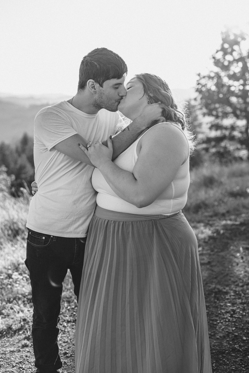 An intimate black and white portrait of a couple sharing a tender kiss on a mountain trail.