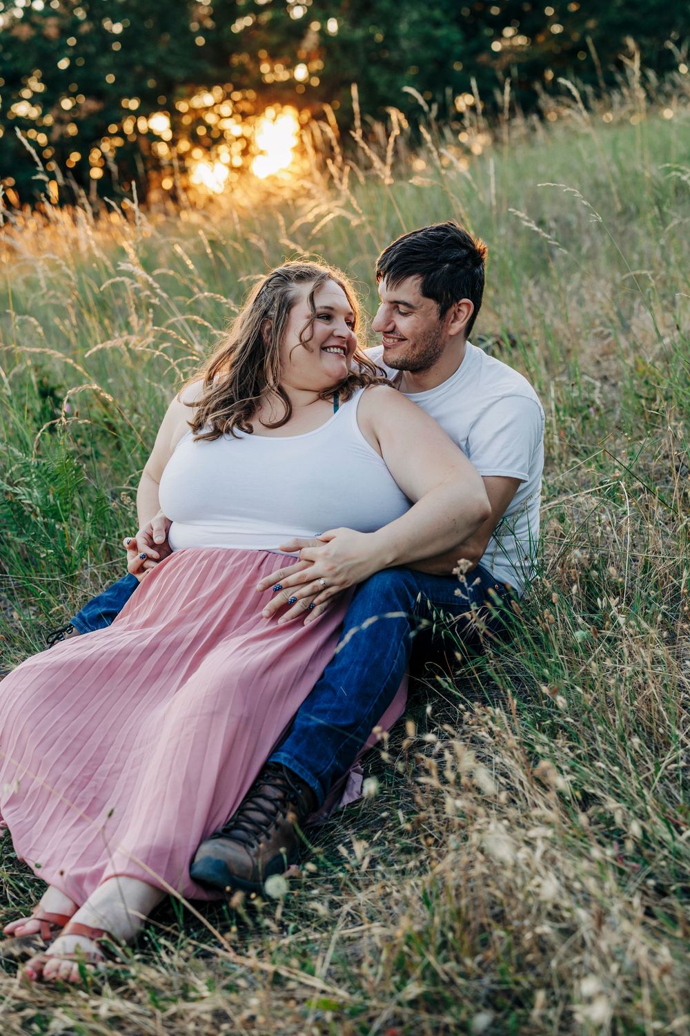 An intimate couple shares a loving moment while sitting in tall grass during golden hour.