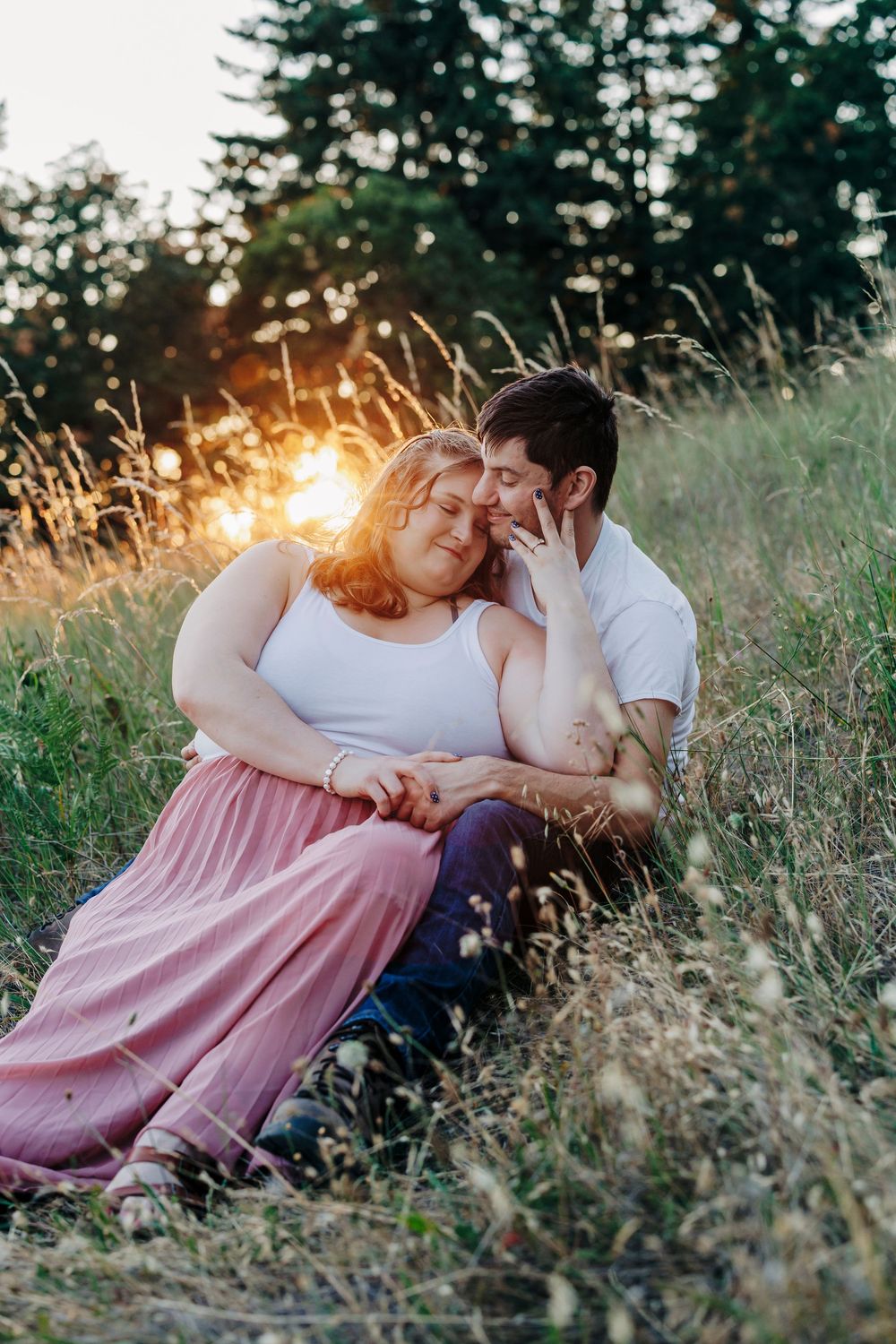 Couple relaxes together in tall grass during sunset, creating an intimate outdoor portrait.