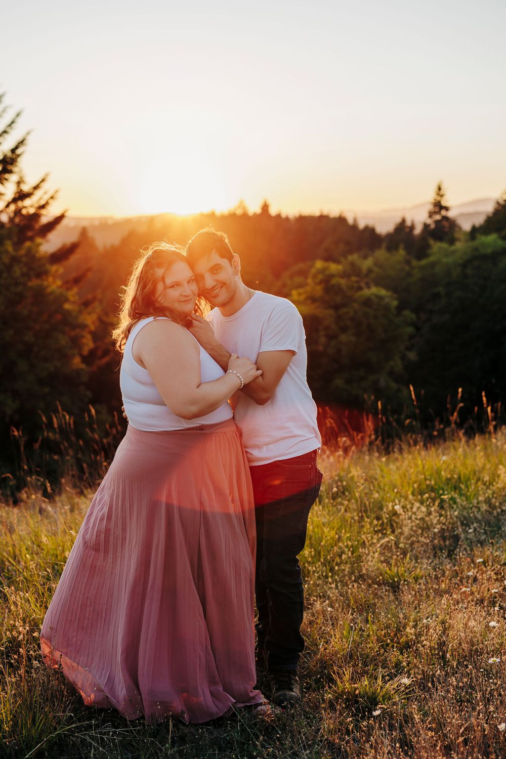 A sunset photoshoot in a hilltop meadow capturing a romantic moment against mountain silhouettes.