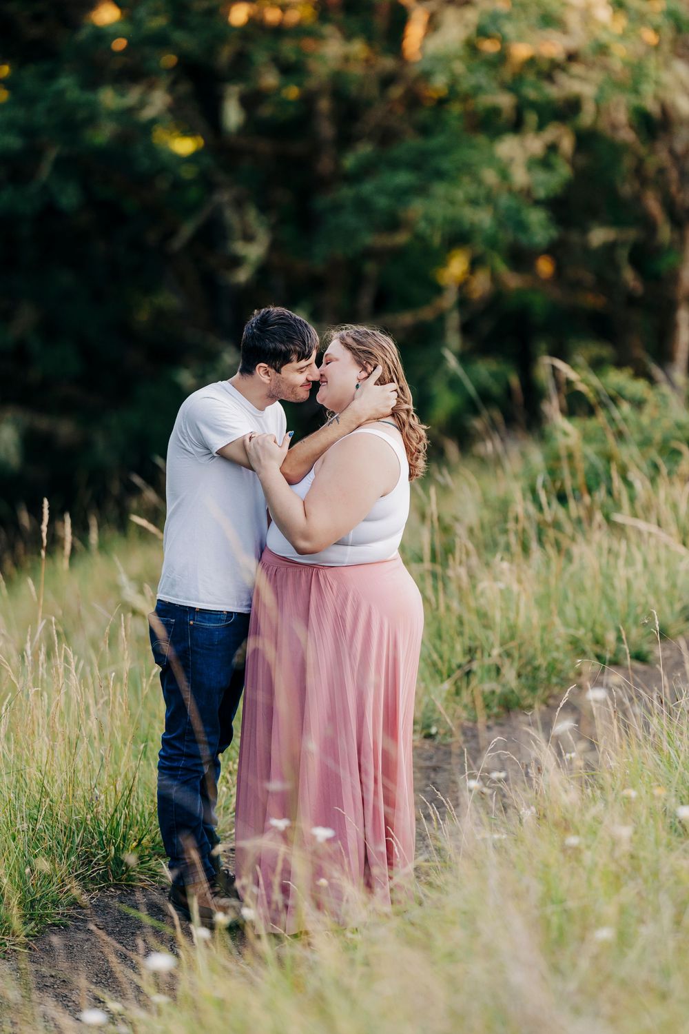 An intimate moment between a couple standing in tall grass with a soft forest backdrop.