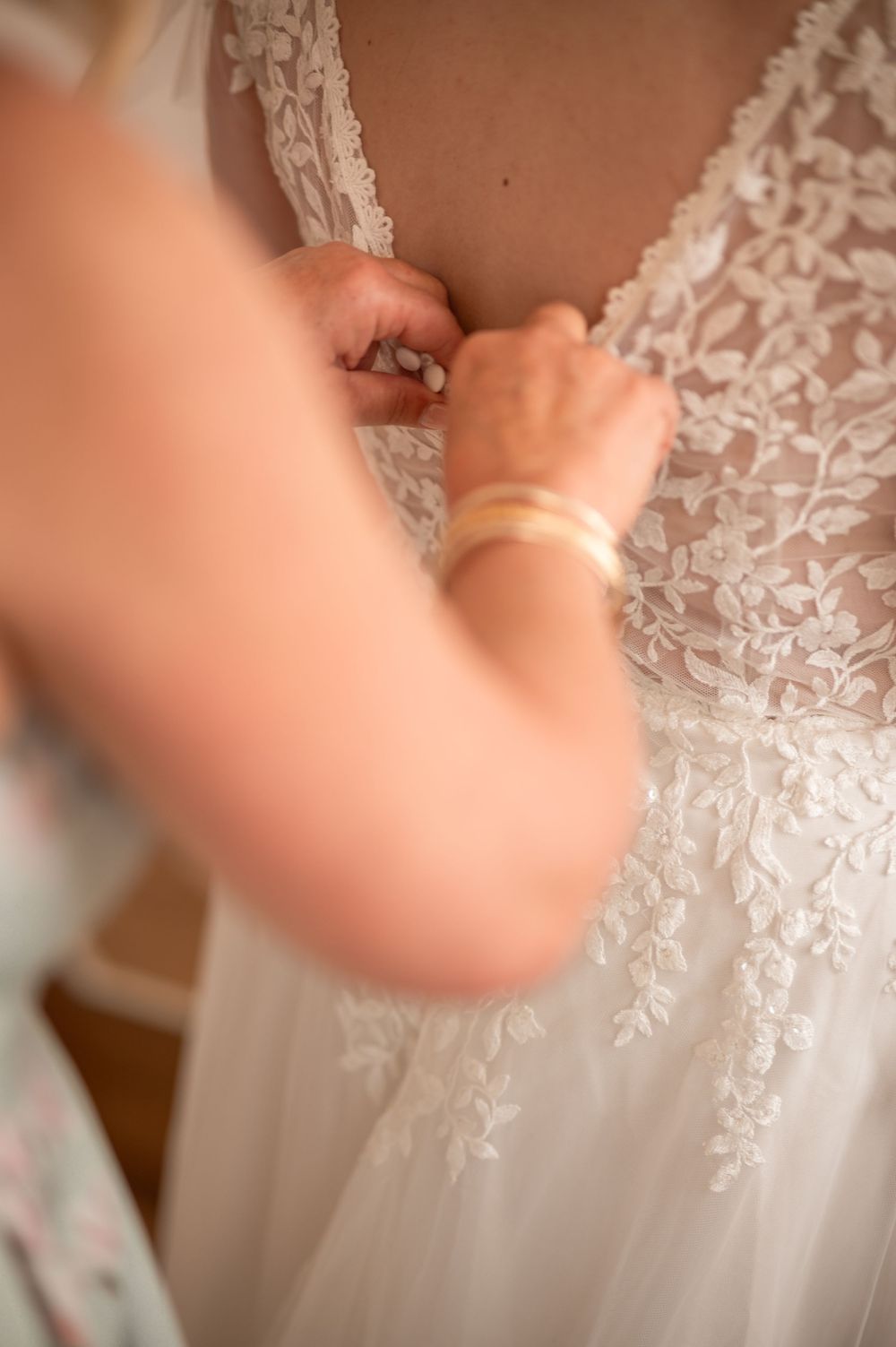 Derniers ajustements de la robe de mariée par la maman, dans une lumière douce.