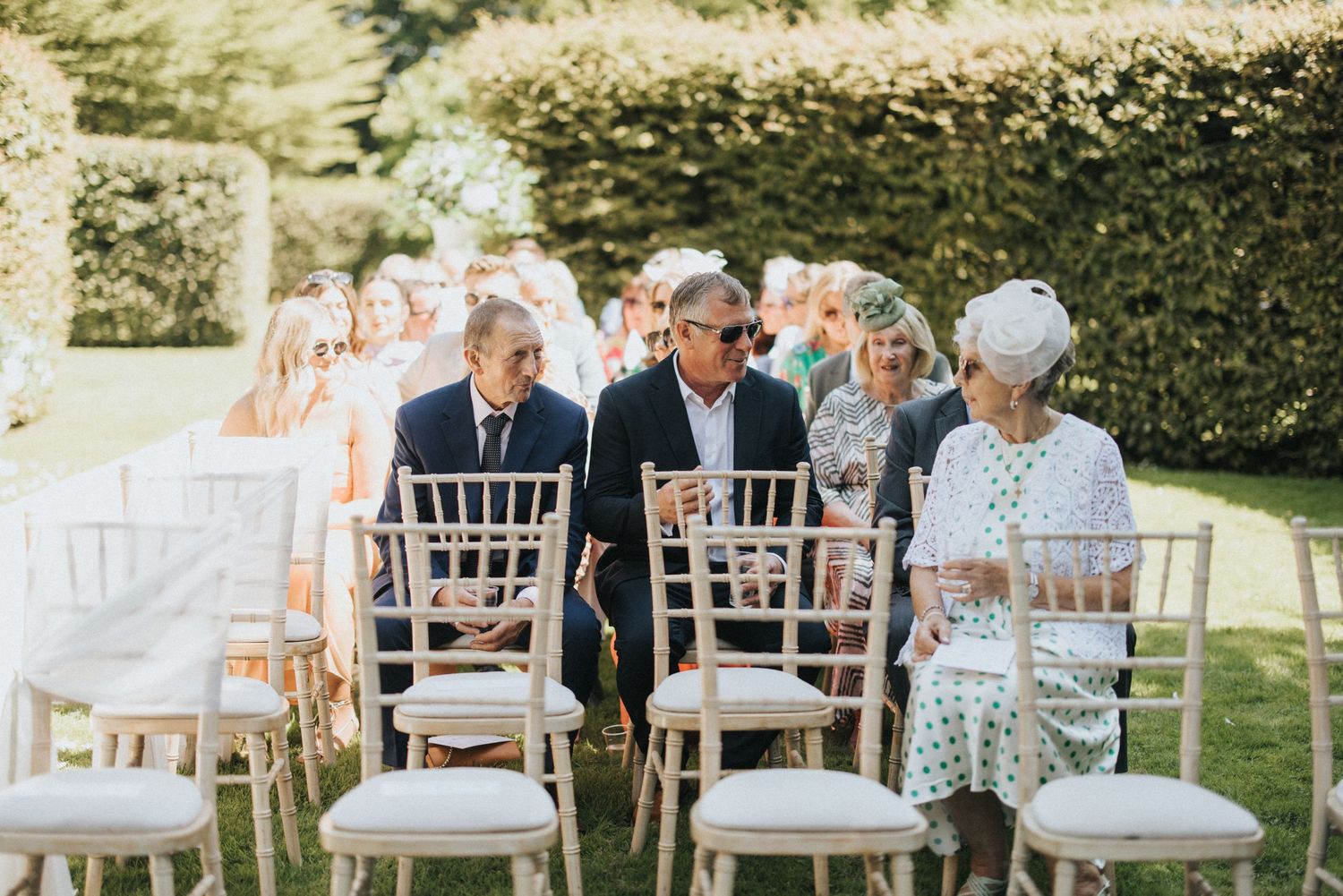 Guests seated in elegant white chiavari chairs during an outdoor garden wedding ceremony at Saltmarshe Hall - taken by Grimsby photographer.