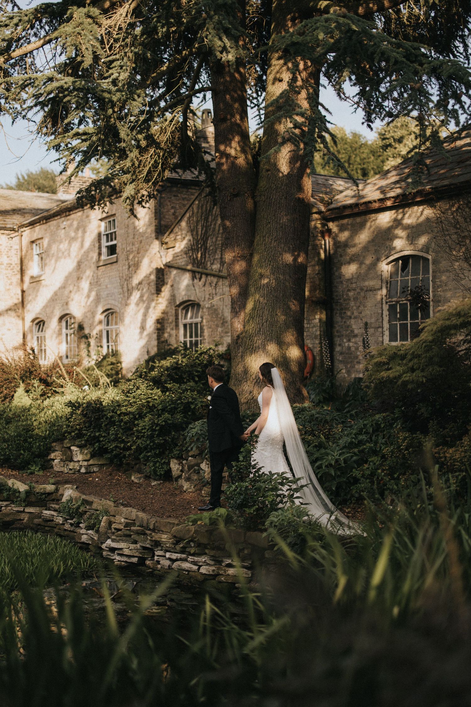 A couple in wedding attire stands outside Saltmarshe Hall surrounded by lush greenery - taken by Grimsby photographers.