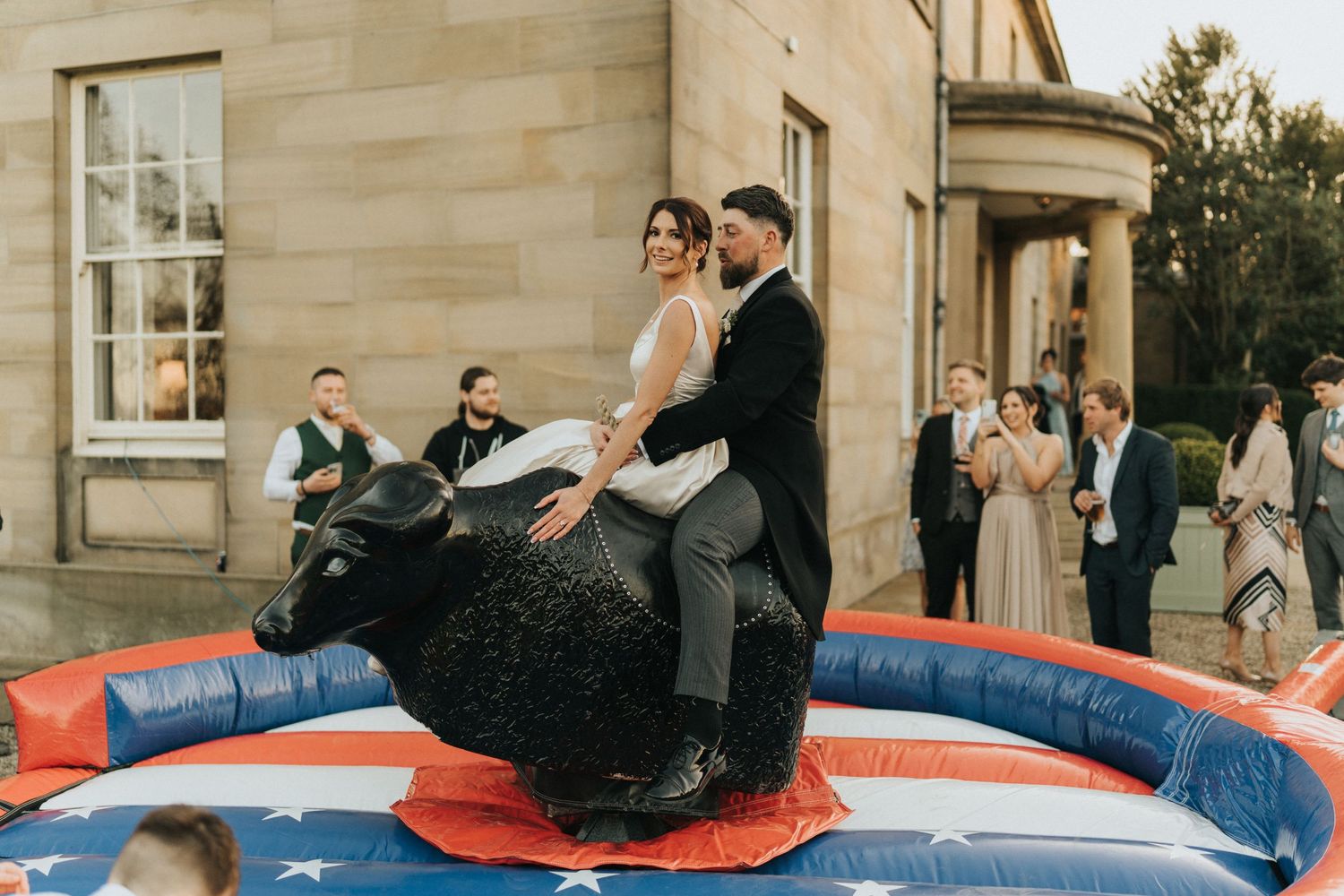 Couple rides mechanical bull at outdoor wedding celebration at Saltmarshe Hall - taken by Grimsby photographer.