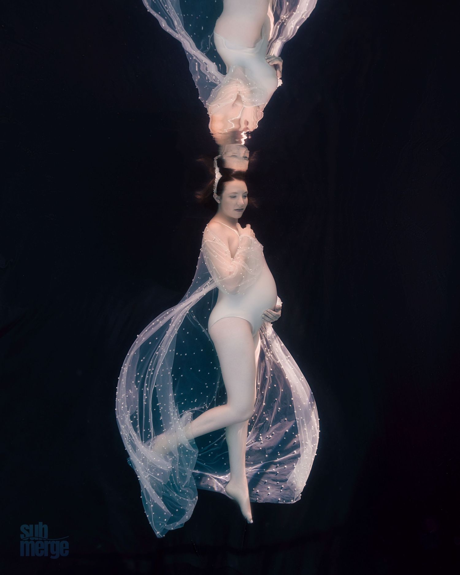 Ethereal underwater photograph of floating figures in white flowing fabric against a dark background.