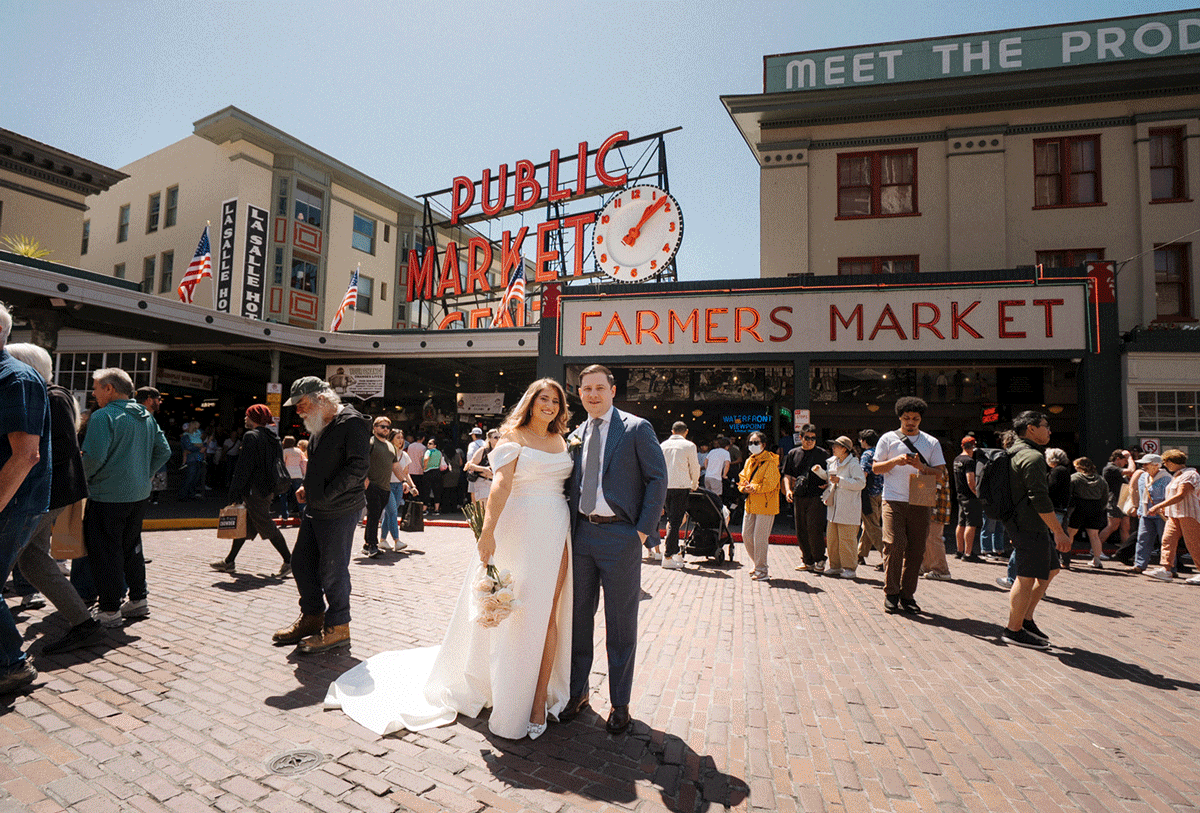 Busy scene at Pike Place Market in Seattle with crowd gathered under iconic public market sign and brick pavement.
