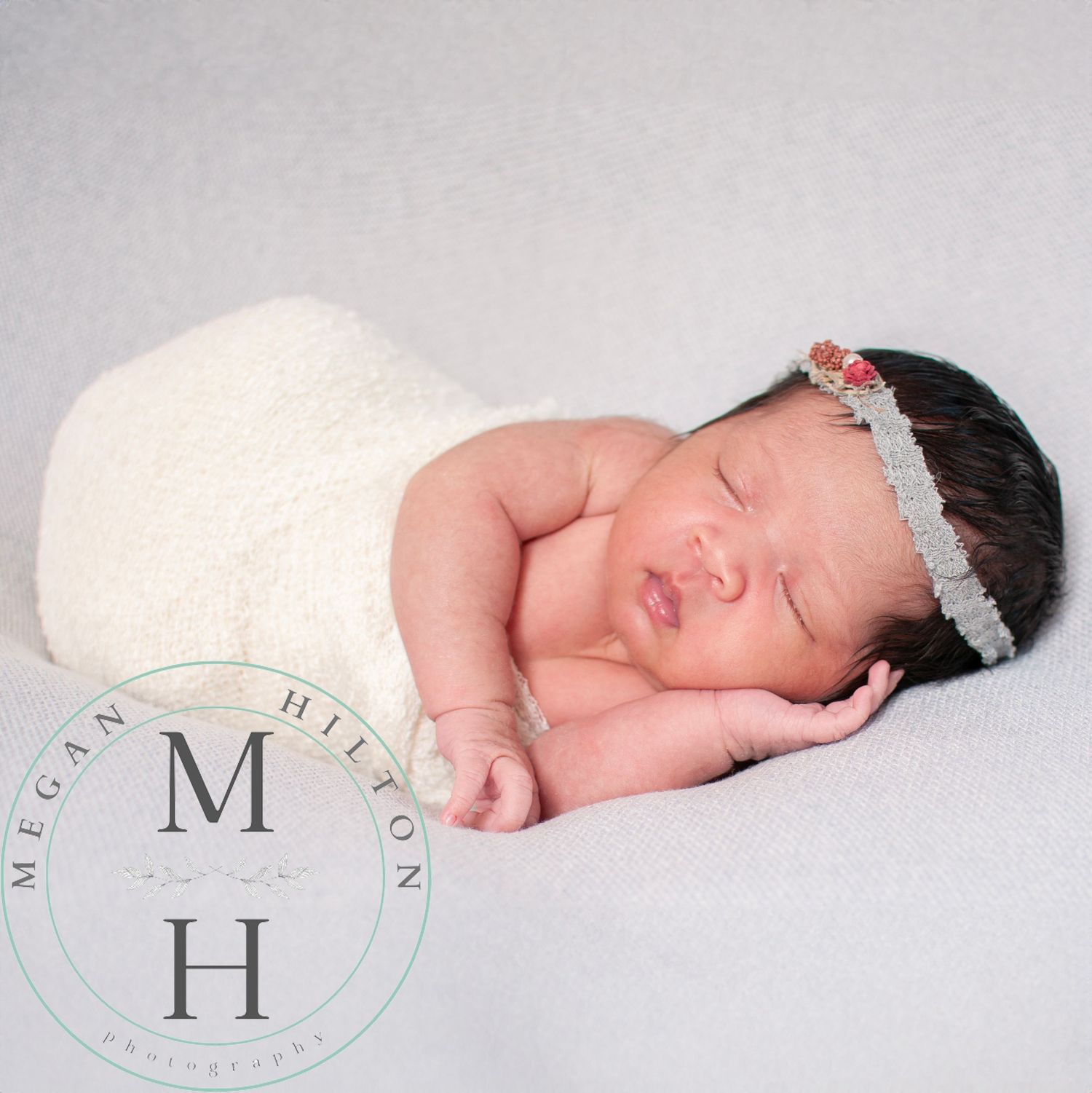 Photo of a peaceful sleeping newborn baby wrapped in ivory with a boho style headband.