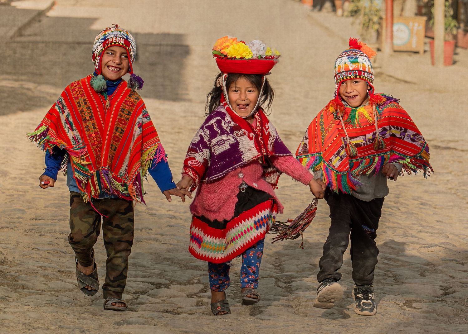 Someone wearing a colorful traditional Peruvian beanie with intricate patterns and tassels smiles behind their hand.