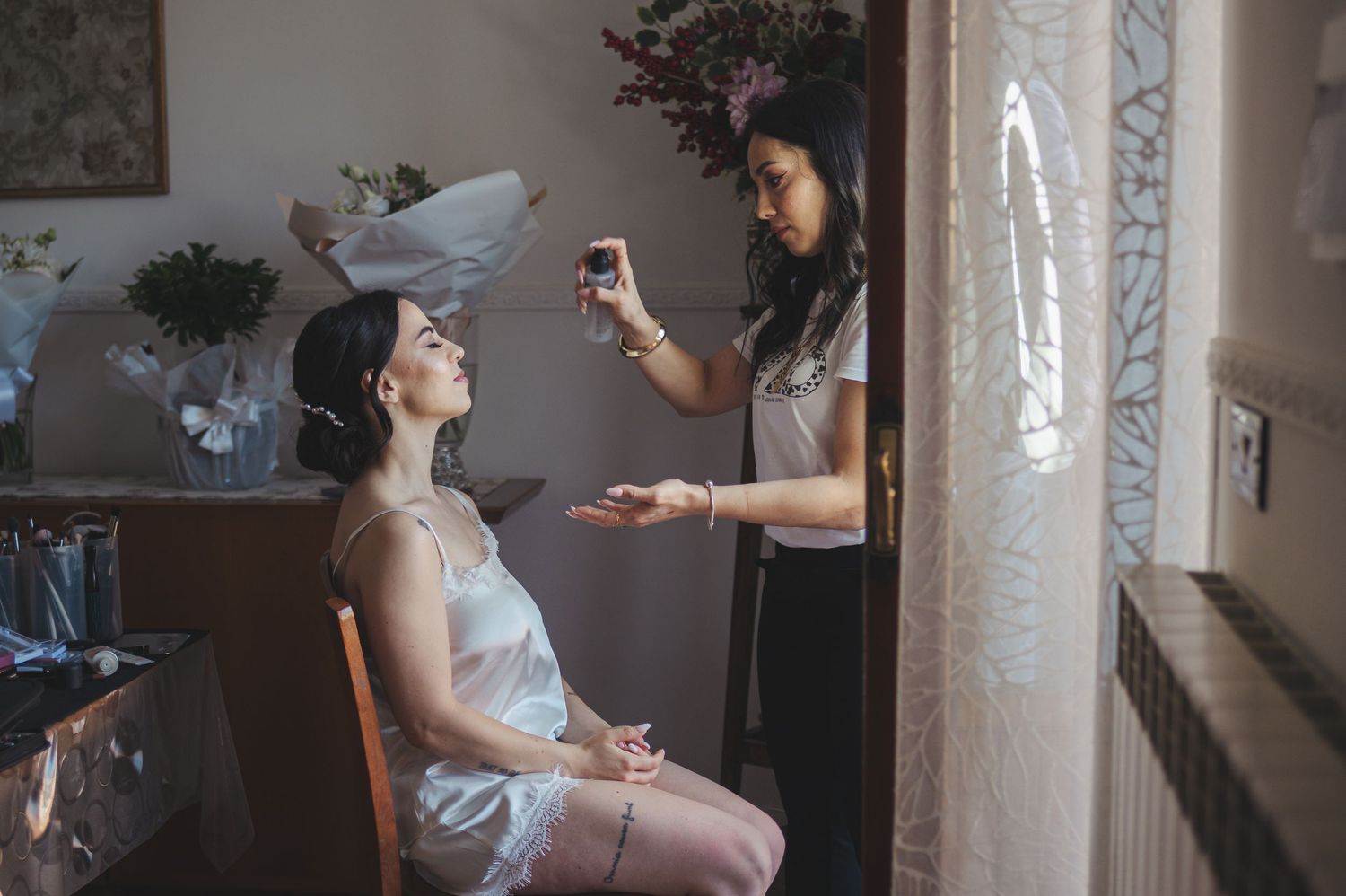 Wedding preparation scene with hairstyling and makeup in a softly lit room.