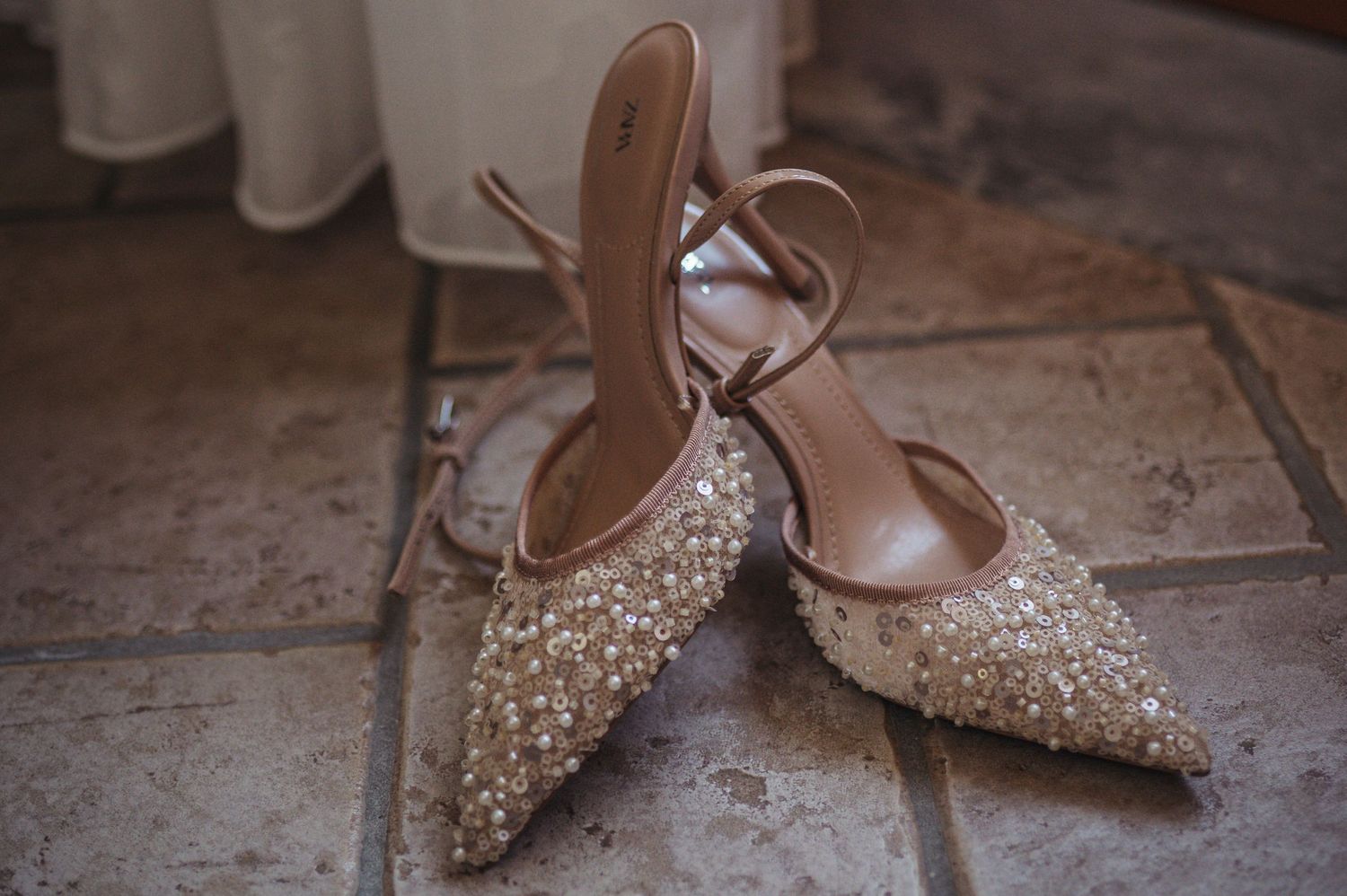 Sparkly beige pointed-toe bridal shoes with crystal embellishments on tile floor.
