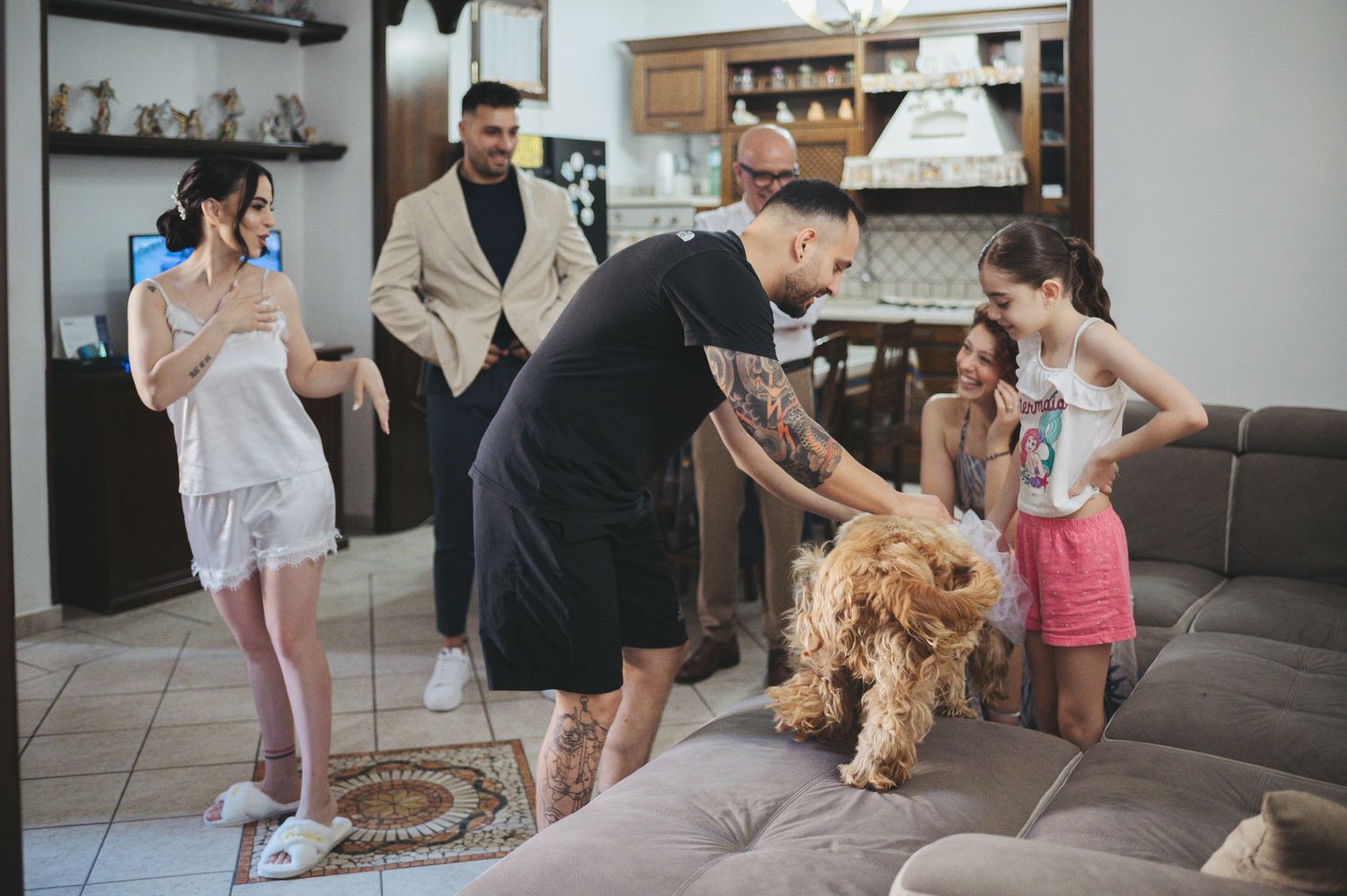 Family and children playing with a dog on a gray sectional couch in a living room.