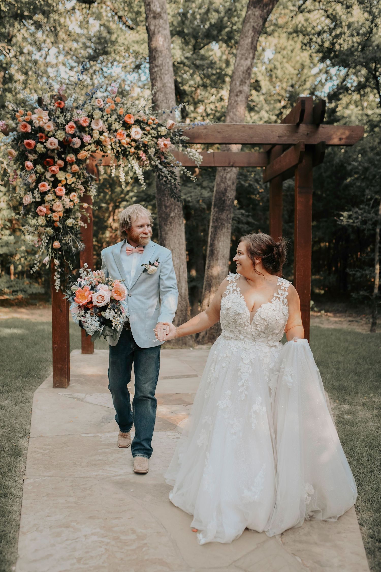 Bride and groom bathed in warm sunset light, standing beneath tall trees