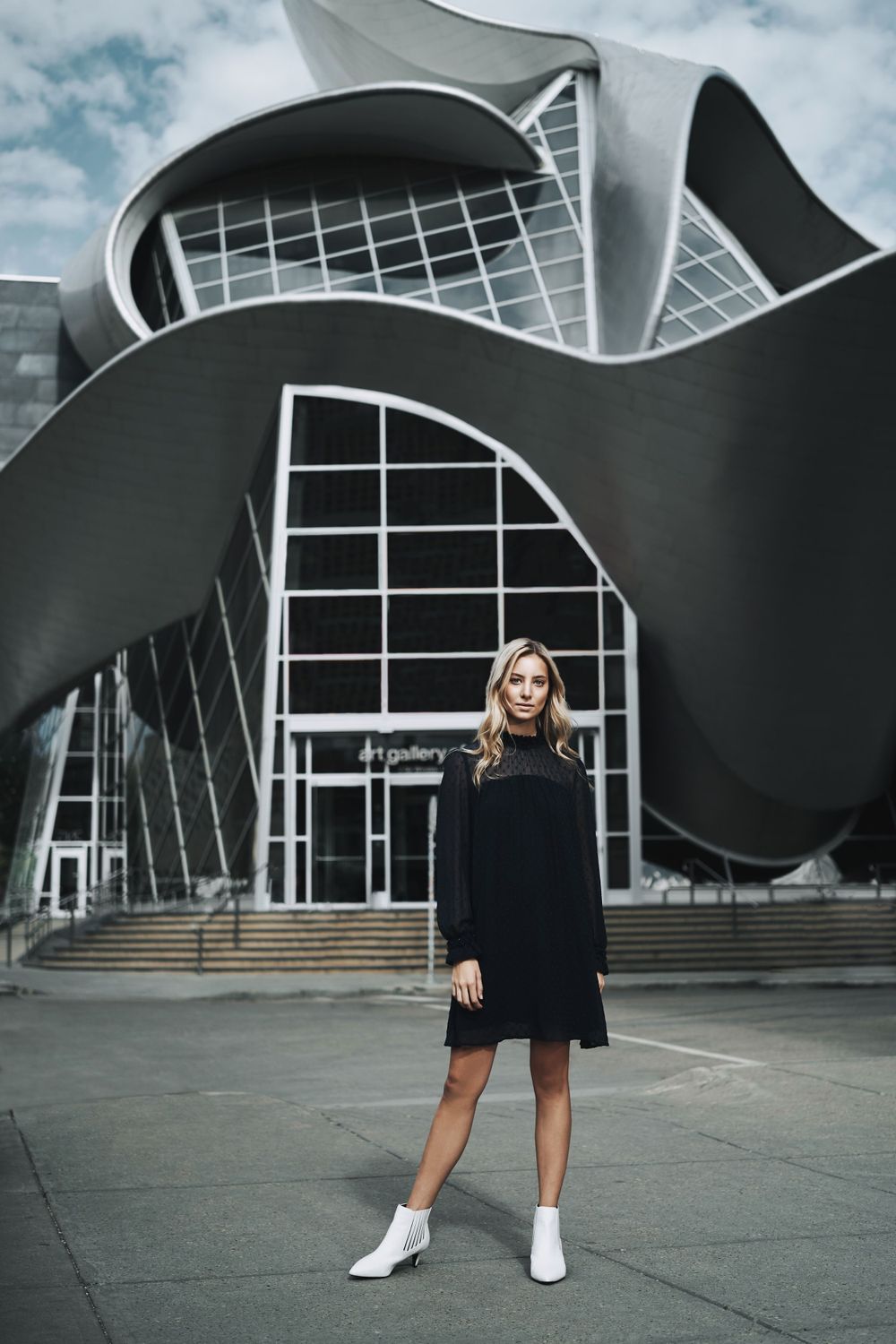 Modern architectural building with curved lines and glass windows serves as backdrop for street style fashion photographed by Evan Will