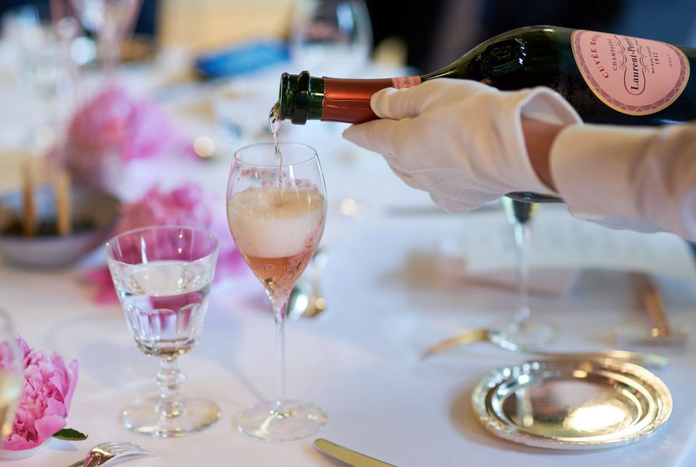 Someone pours pink sparkling wine into elegant glasses at an elegant table setting with floral decor.