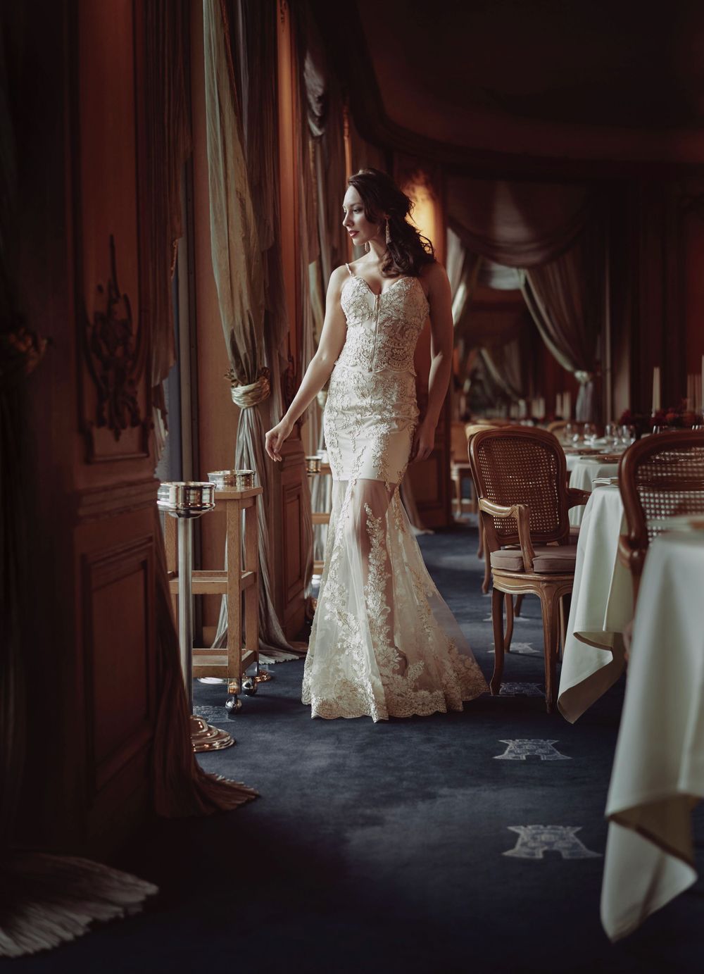 A bride in a fitted lace wedding gown stands elegantly in a luxurious dining room with ornate decor photographed by Evan Will of Sharko