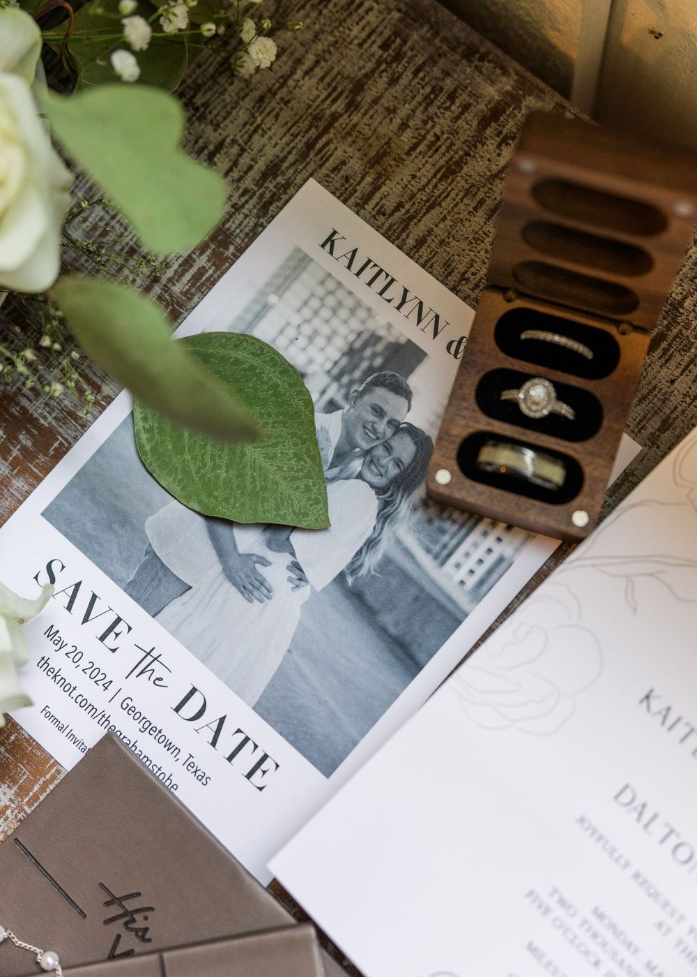 A save the date wedding invitation with green foliage and vintage decor elements on a rustic wooden surface.