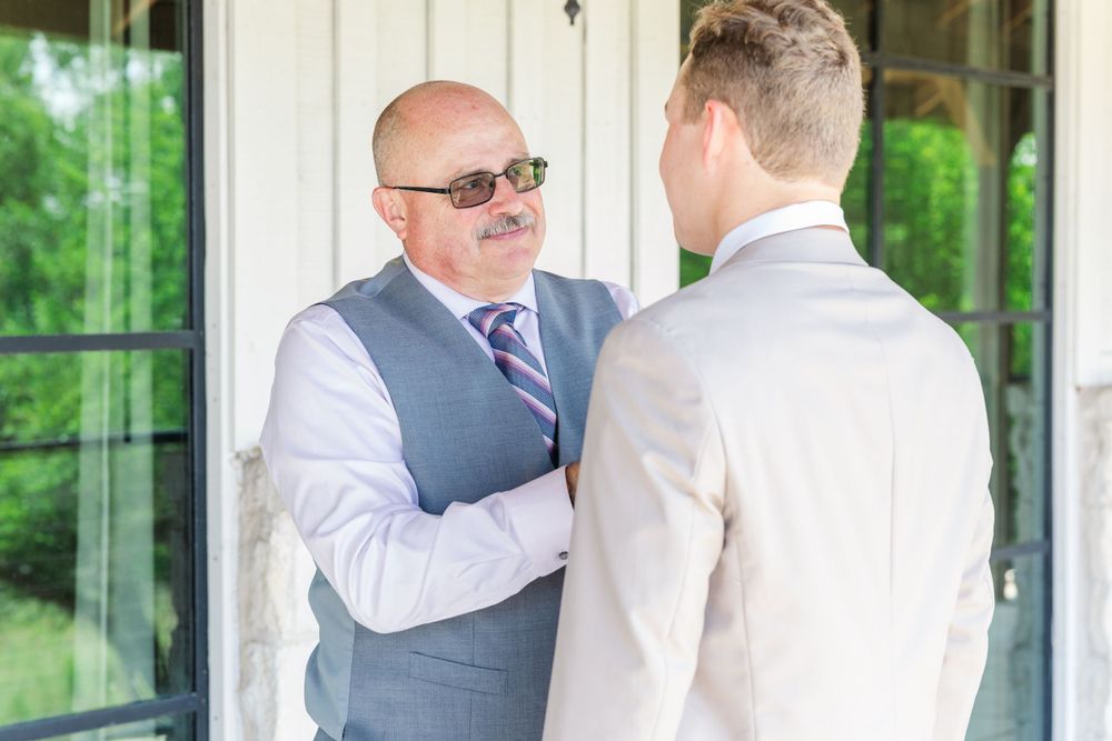 Two men in formal attire having a conversation outside a building with glass doors on a sunny day.