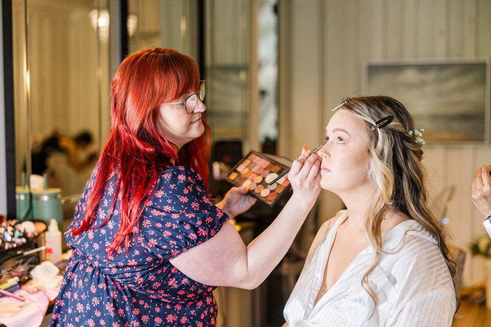 A makeup artist applies cosmetics during wedding preparation in a brightly lit room.