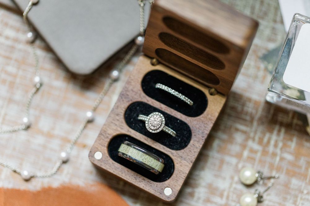 Close-up view of a wooden ring box with an elegant diamond engagement ring nestled in black velvet.