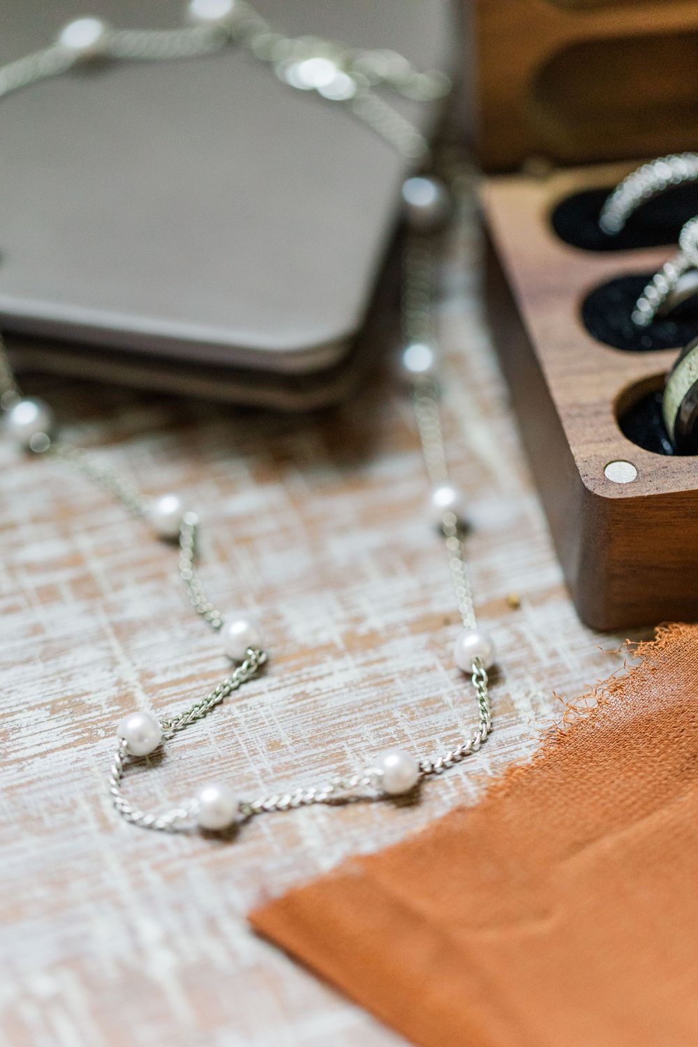 A delicate pearl necklace and silver jewelry items displayed on a rustic wooden surface.