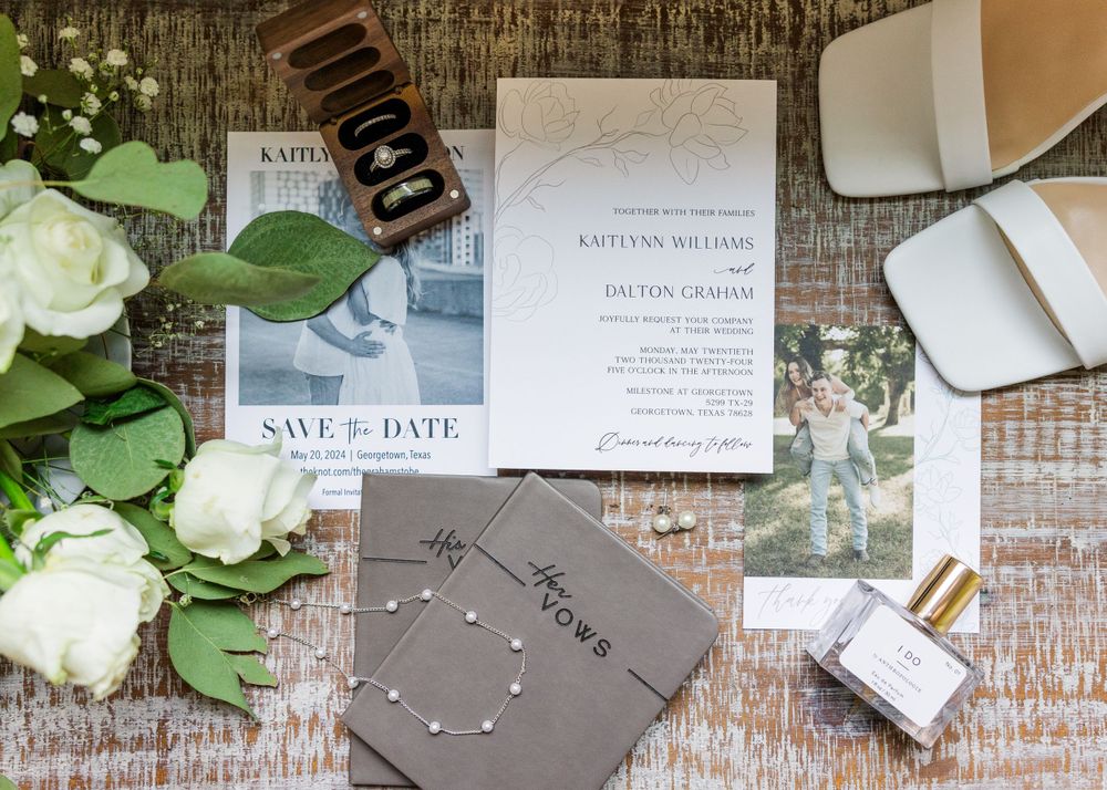Wedding stationery flat lay with save the date cards, floral elements and perfume on rustic wood.