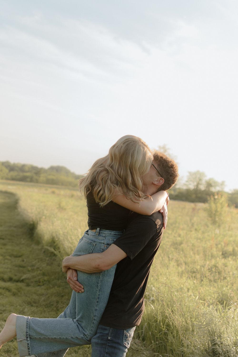 Two people embracing in a sunny meadow with tall grass at golden hour.
