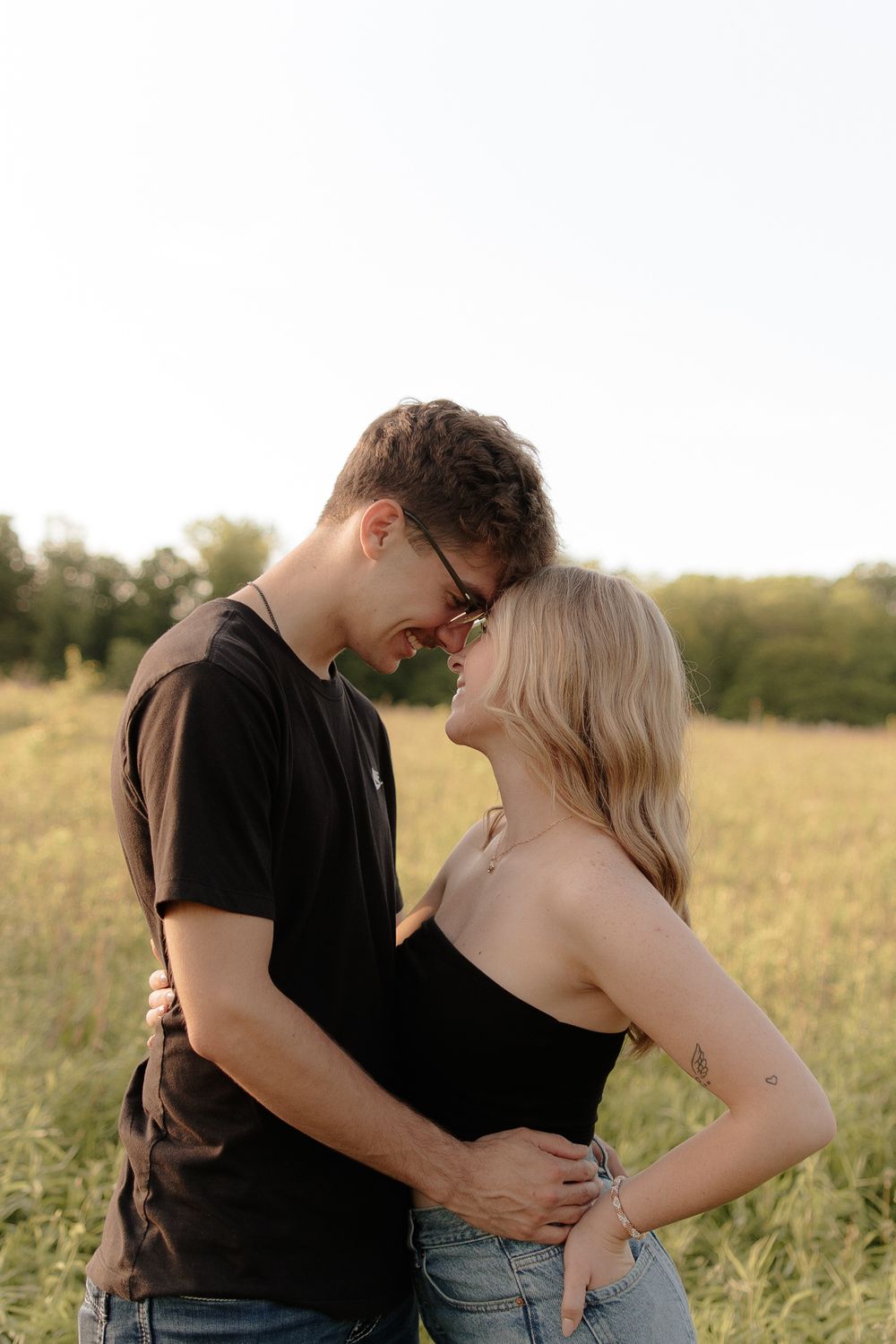 Romantic couple embraces in a sunlit meadow during golden hour, sharing an intimate moment among tall grass.