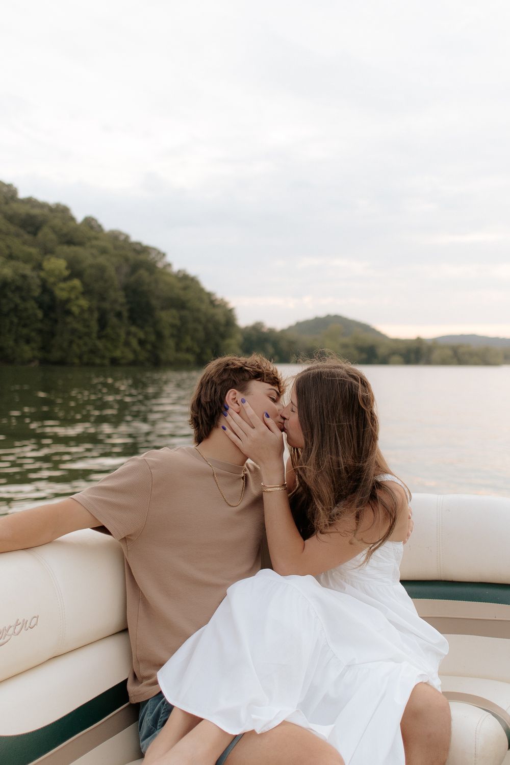 A romantic moment shared between a couple on a boat with a scenic lake and wooded shoreline in the background.