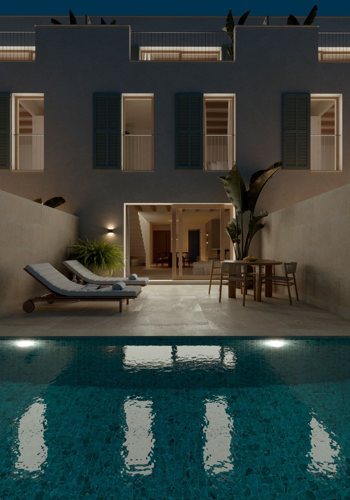 Modern courtyard with illuminated swimming pool, lounge chair, and outdoor dining area against white architectural facade at night.