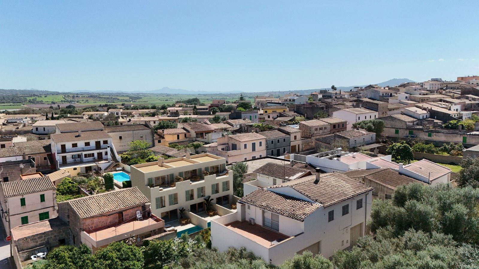 Expansive aerial view of a Mediterranean hillside town with terracotta roofs and stone buildings under blue skies.