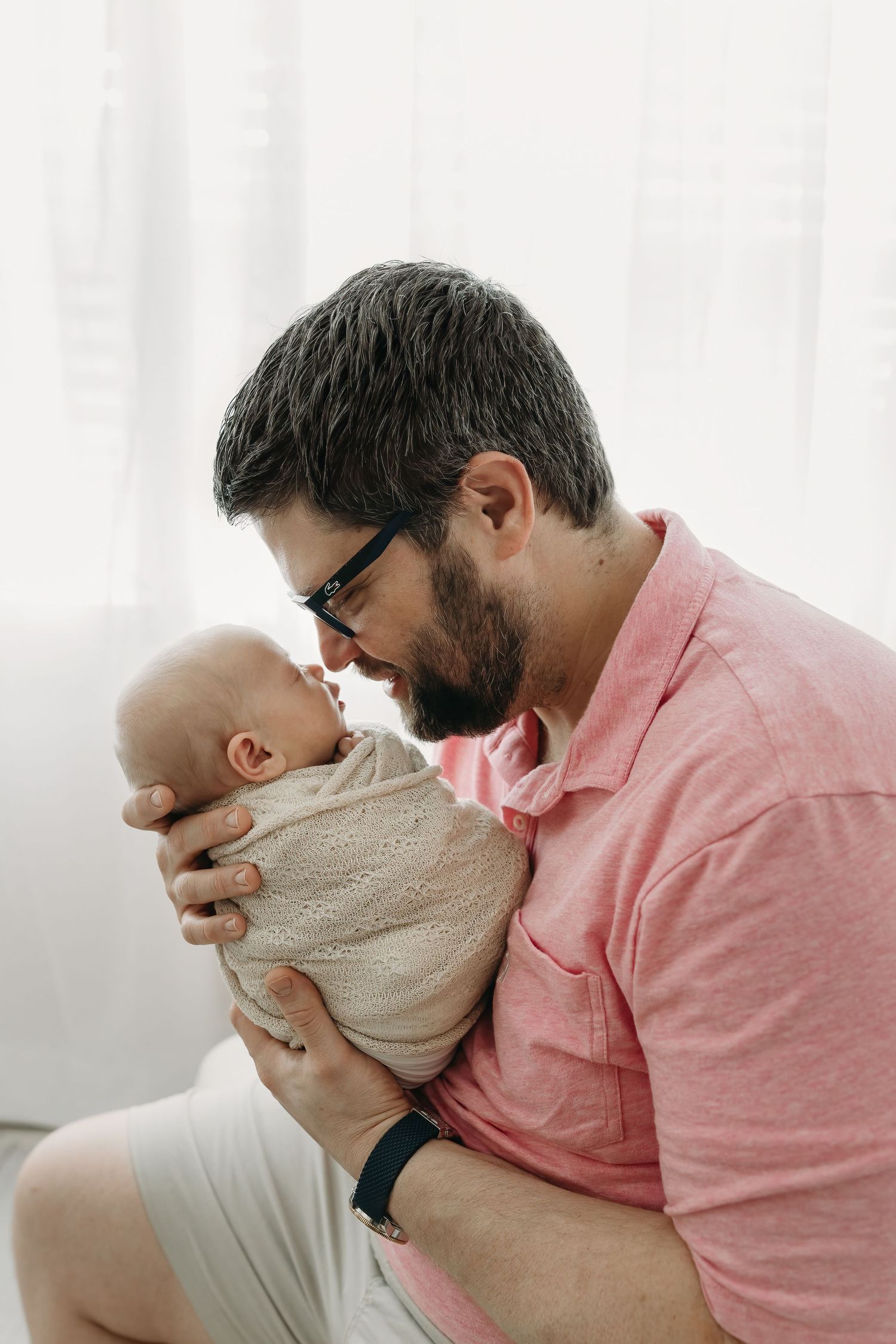 A dad in glasses and pink shirt shares a tender moment with a swaddled baby girl during tampa newborn photos