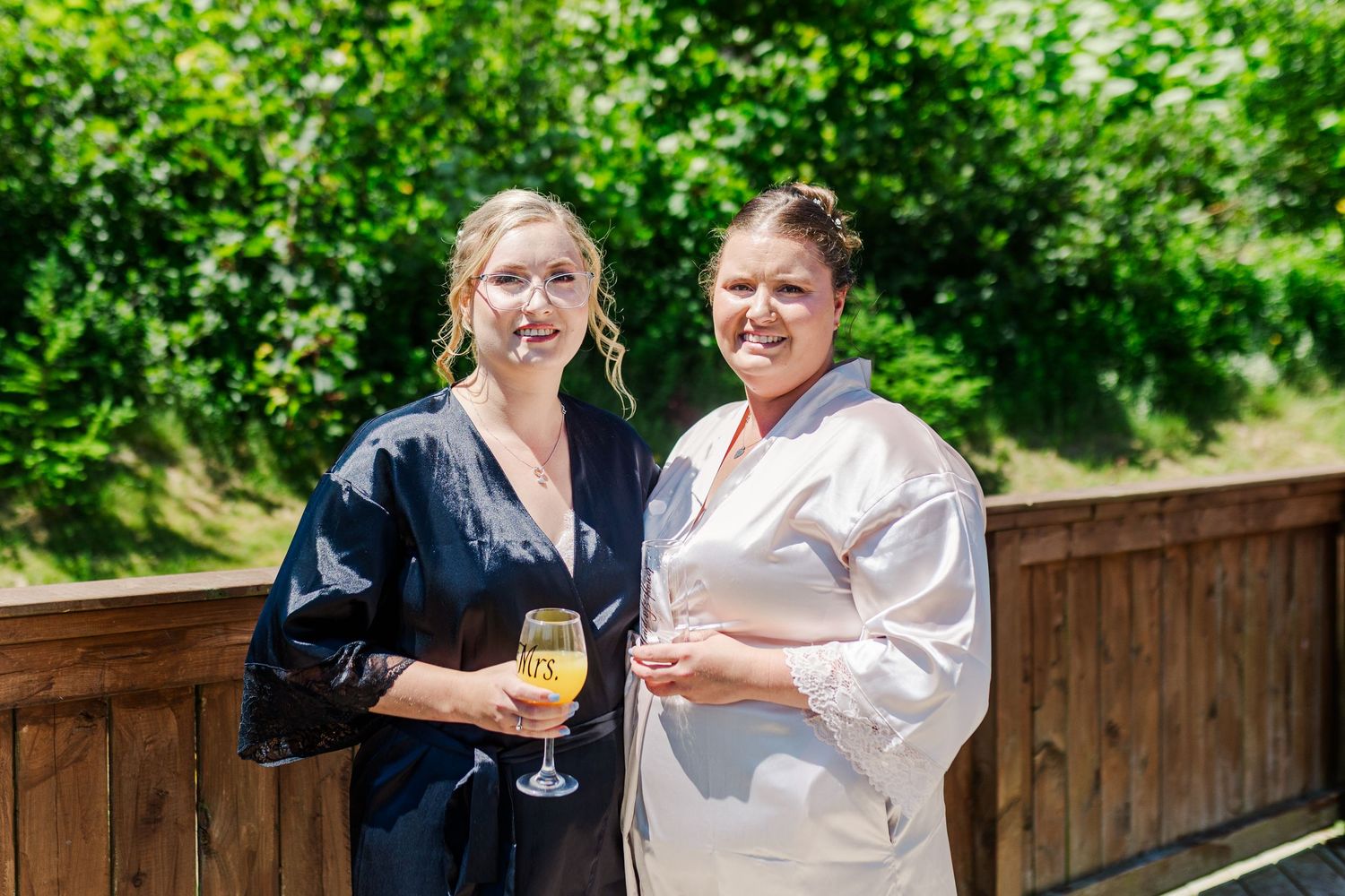 Two people enjoy a celebratory toast outdoors on a sunny day with green foliage in the background.