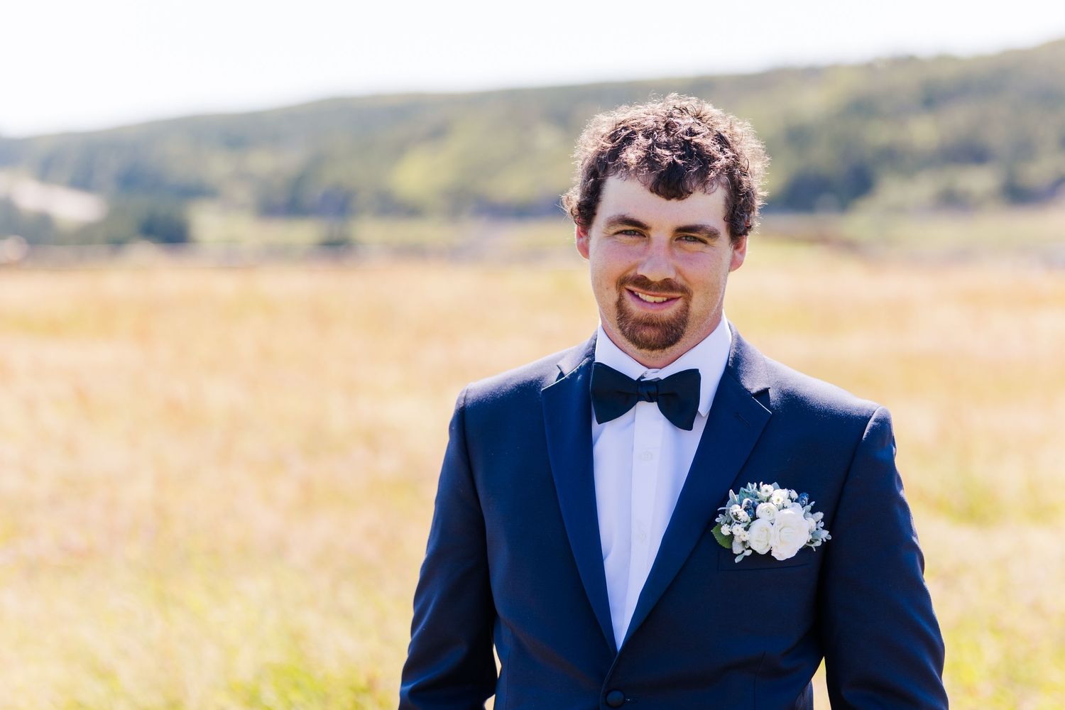 Wedding party in navy blue suits and white shirts walk through a golden field during sunset.