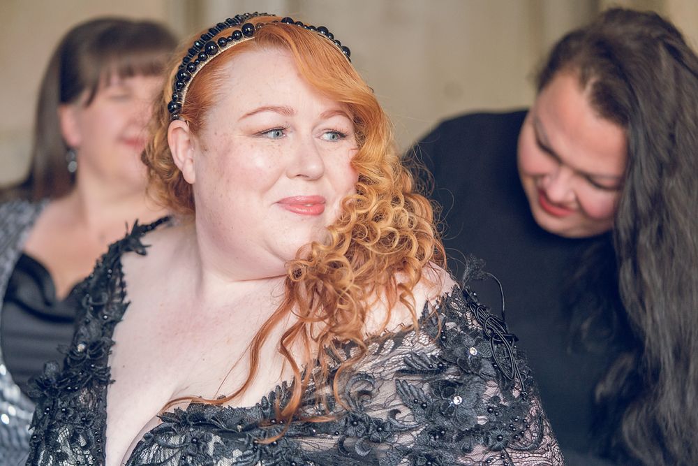 Person with curly red hair and sparkly black dress smiling at formal event.