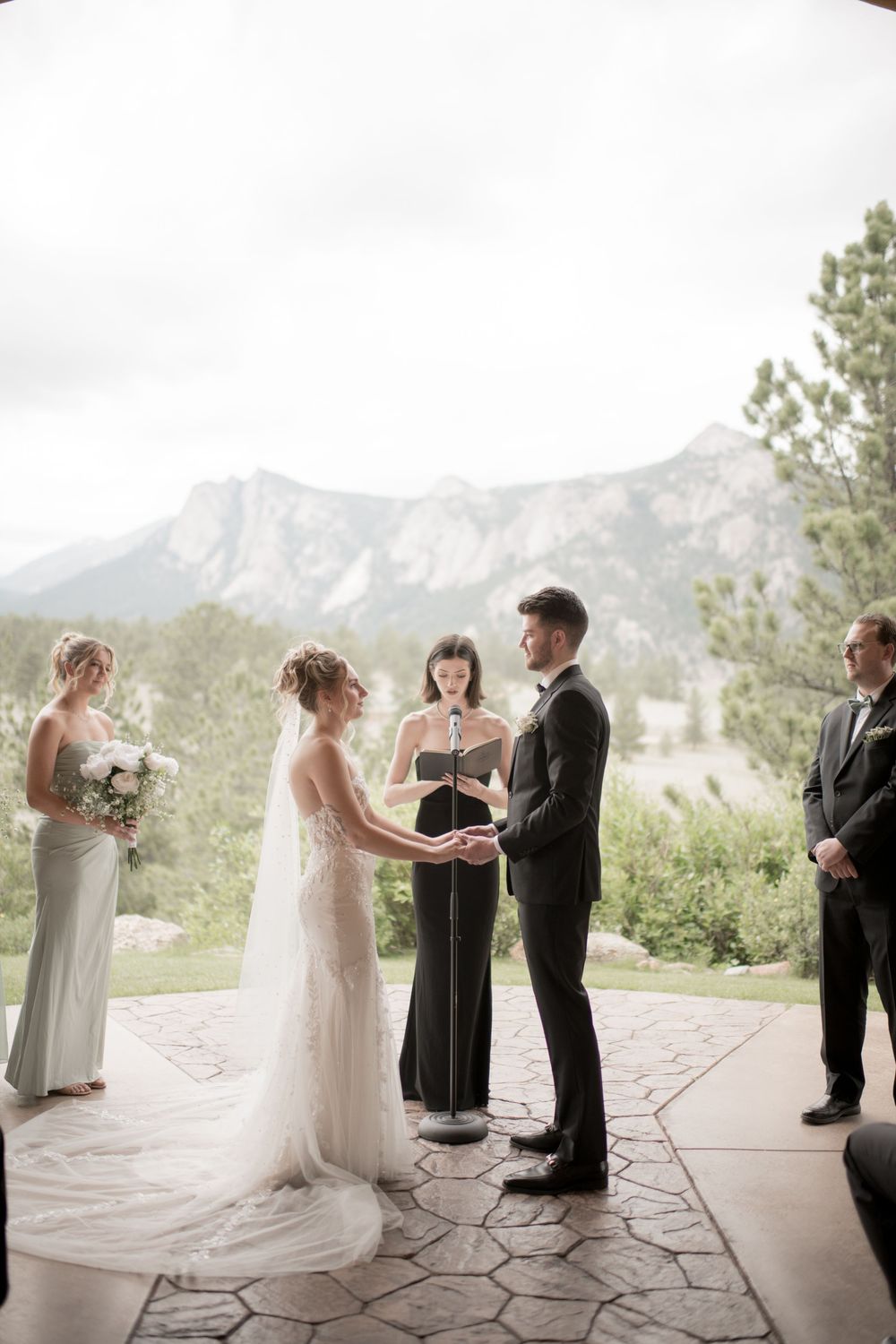 Mountain wedding ceremony taking place on a stone patio with majestic peaks in the background on an overcast day.