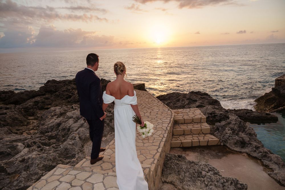Couple standing on stone pathway overlooking ocean sunset view.