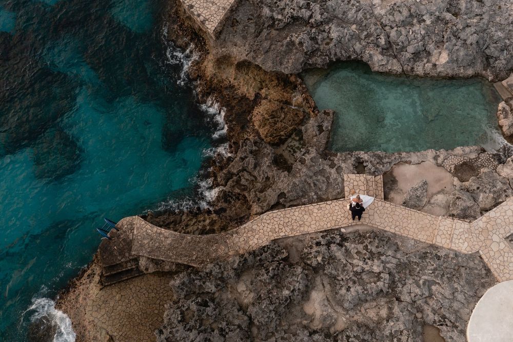 Scenic aerial view of a coastal path along rugged cliffs with turquoise waters and someone walking along the trail.