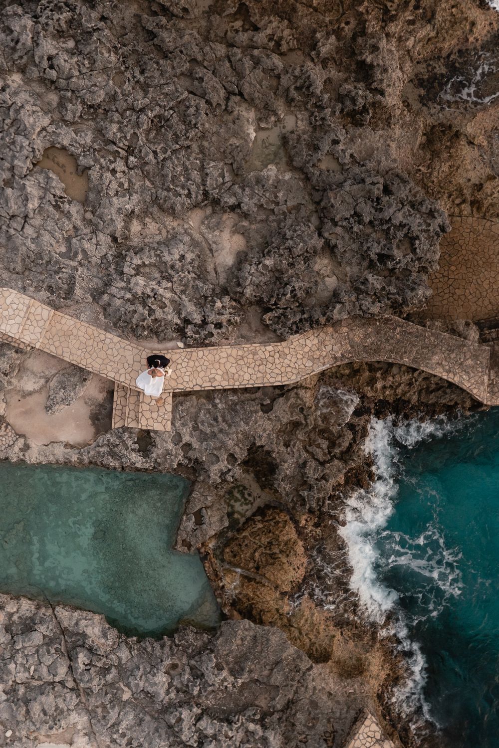 Aerial view of a wooden boardwalk crossing over turquoise waters and rocky coastal terrain.