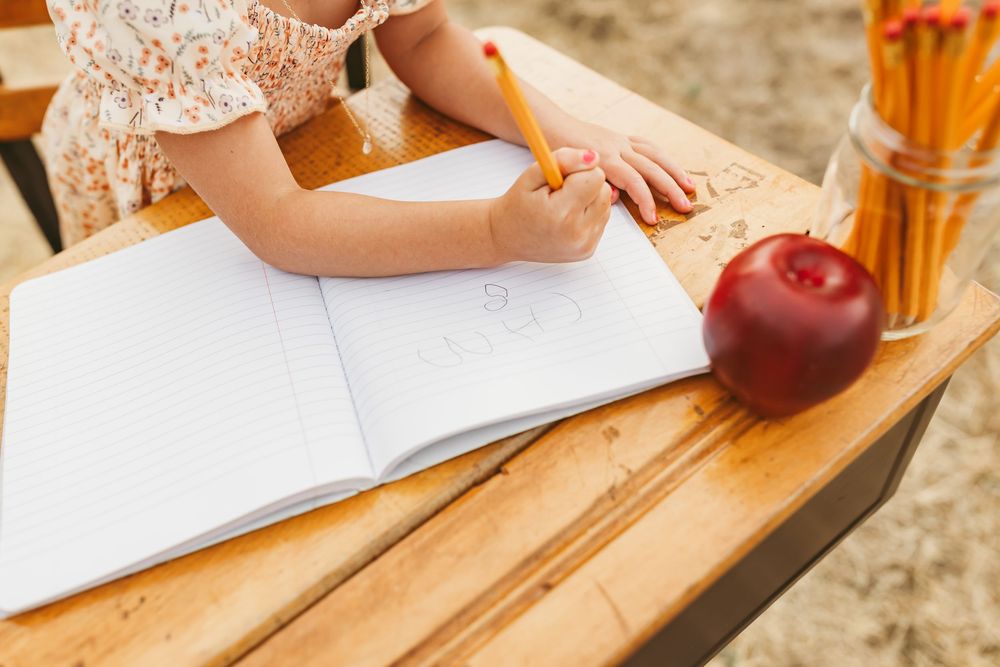 Close up of hands writing in a notebook on wooden table with red apple and drink in view.