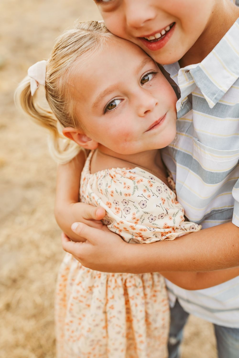 Two young children share a sweet moment together outdoors in soft lighting.