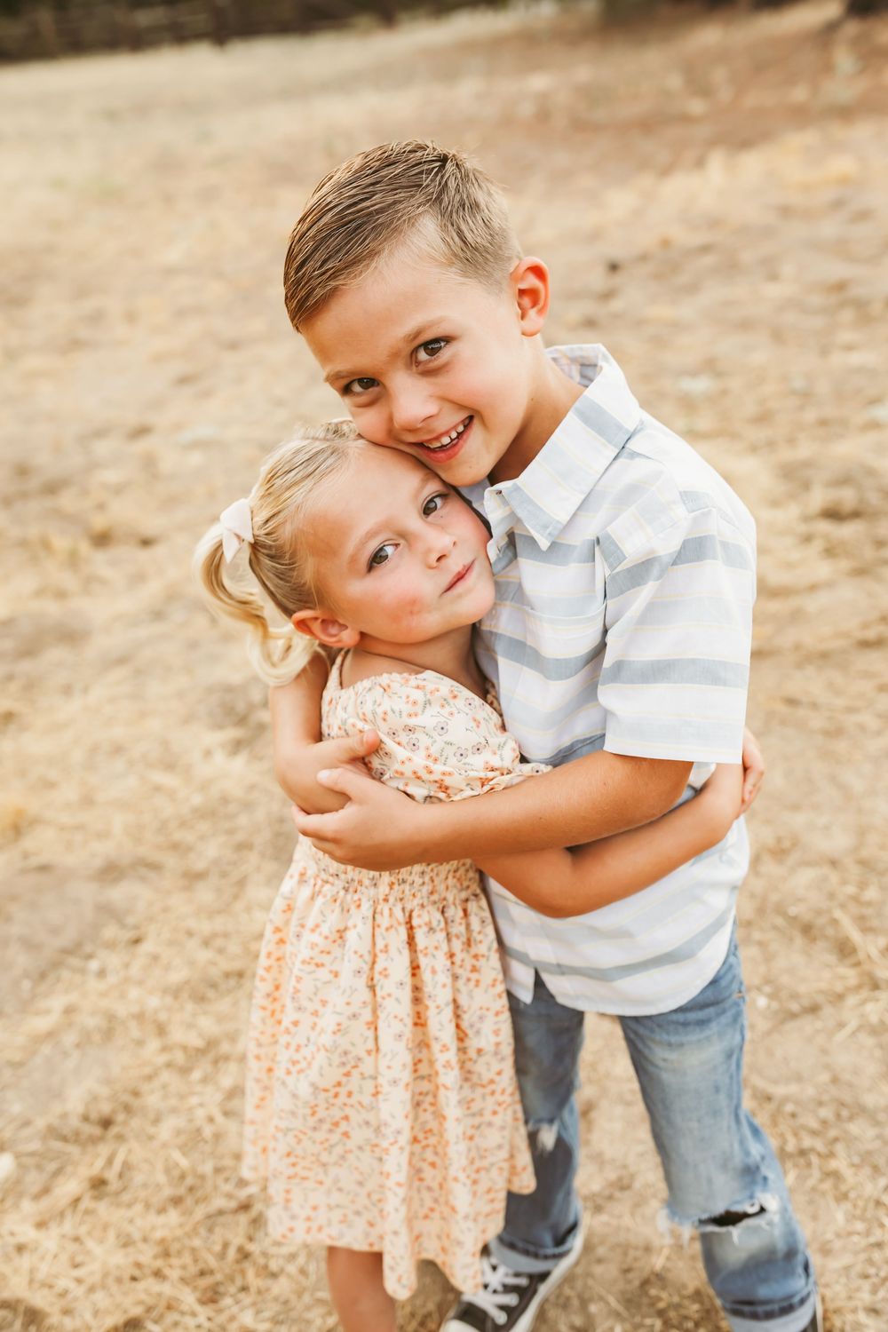 Two children embrace playfully while standing in a sunny outdoor setting.